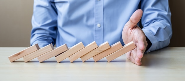 Mano dell&#39;uomo d&#39;affari che arresta i blocchi o domino di legno di caduta