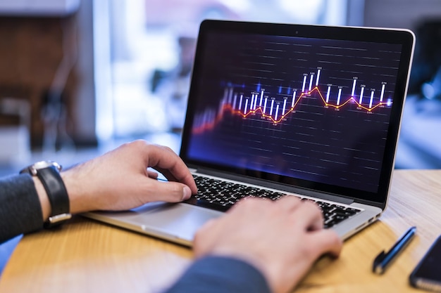 Mano dell'uomo d'affari che digita sul computer portatile della tastiera con l'ologramma dei grafici di affari