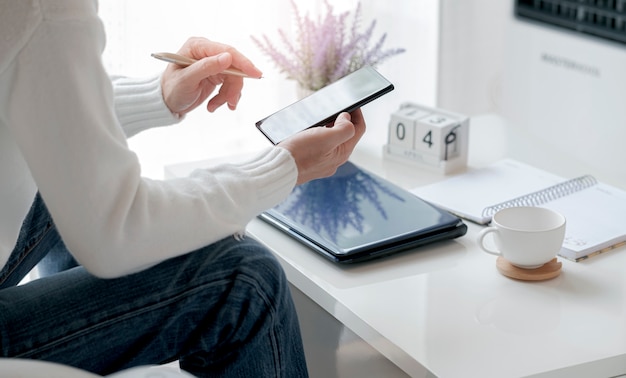 Mano dell'uomo del primo piano facendo uso dello smartphone che lavora dalla casa. Lavoro a distanza.