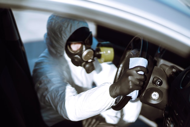 Mano dell'uomo in tuta protettiva lavaggio e disinfezione del volante in macchina.