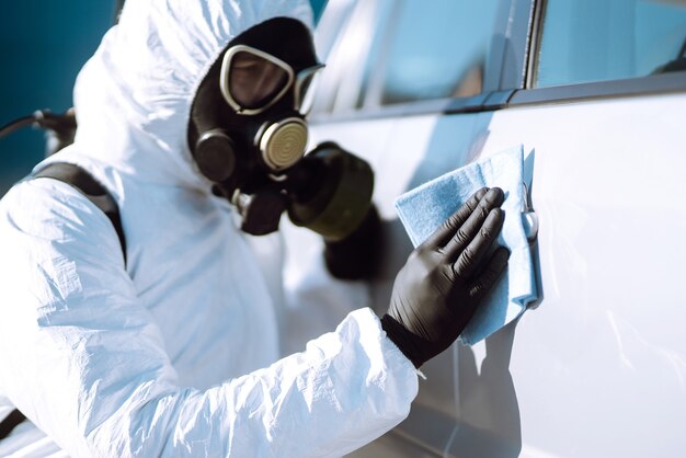 Mano dell'uomo in tuta protettiva per il lavaggio e la disinfezione delle maniglie di un'auto.