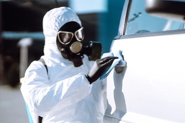 Mano dell'uomo in tuta protettiva per il lavaggio e la disinfezione delle maniglie di un'auto.