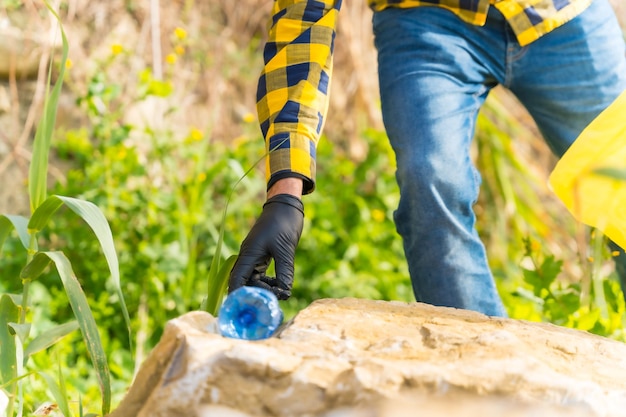 Mano dell'uomo irriconoscibile che raccoglie una bottiglia di plastica in una foresta Riciclaggio del concetto di ecologia