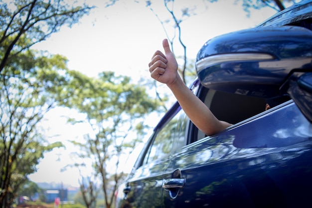 Mano dell'uomo viaggiatore all'interno dell'auto durante il viaggio con il pollice in alto gesto fuori dal finestrino