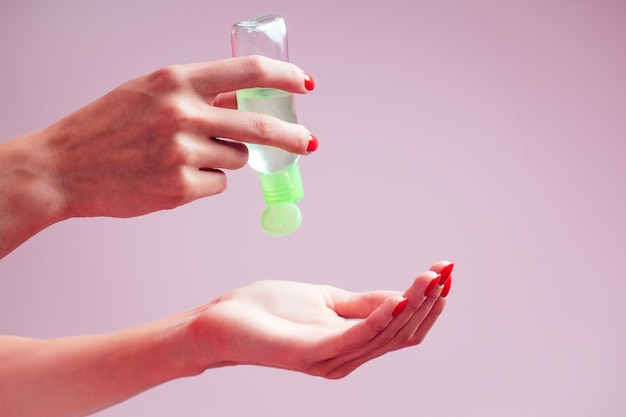 Mano della donna che applica disinfettante per le mani su uno sfondo rosa in studio