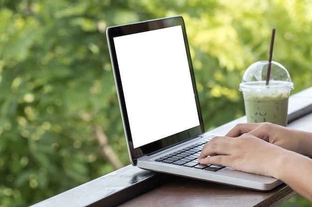 Mano della donna che funziona con il computer portatile e tè verde fresco sullo scrittorio di marrone. sfondo della natura