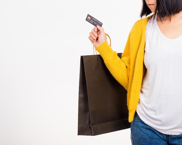 Mano della donna che indossa una camicia gialla con in mano borse della spesa nere e carta di credito