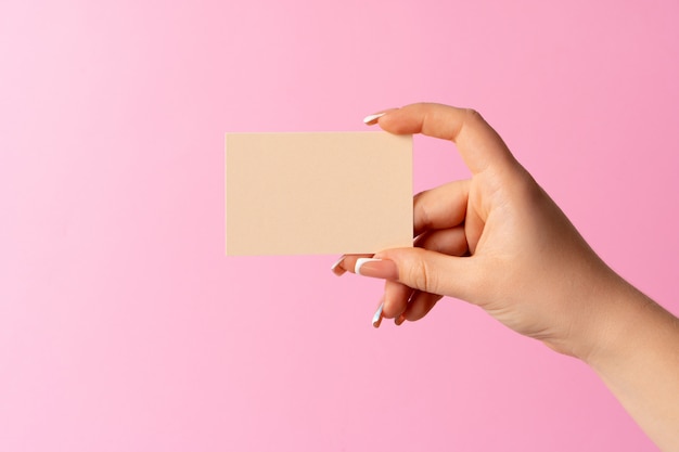 Mano della donna che mostra biglietto da visita in bianco su fondo rosa.