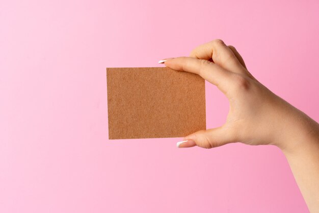 Mano della donna che mostra biglietto da visita in bianco sulla parete rosa.