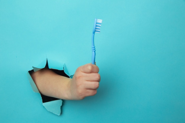 Mano della donna che mostra uno spazzolino da denti da un buco strappato nel muro di carta