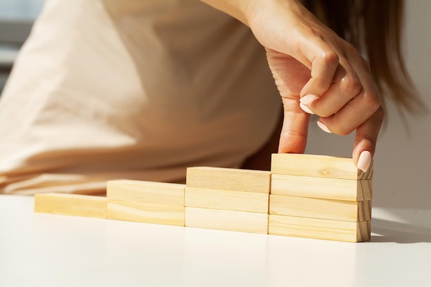 Mano della donna che organizza l'impilamento del blocco di legno come scala a gradini