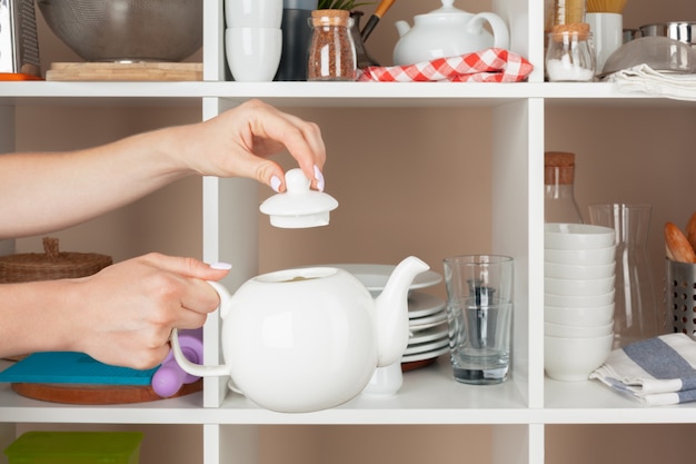 Mano della donna che prende i pezzi delle stoviglie dallo scaffale in cucina