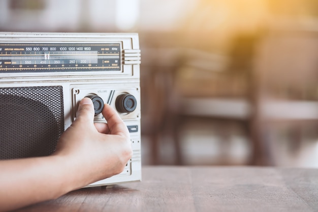 Mano della donna che regola il volume del suono sul retro stereo della cassetta radiofonica nel tono di colore d'annata