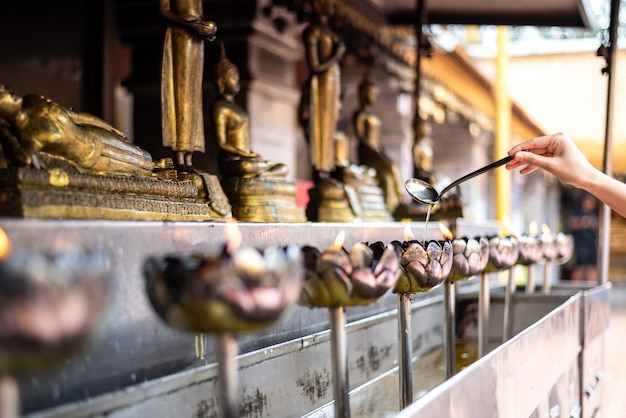 Mano della donna che riempie vecchio in tazza tailandese della candela del metallo di stile in tempio di Doi Suthep, Chiang Mai, Tailandia