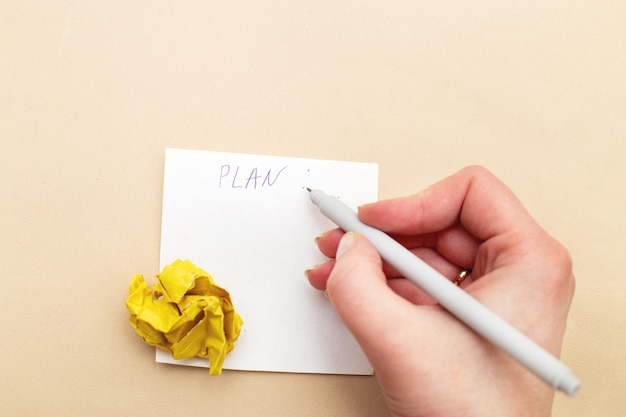 Mano della donna che scrive un piano o una lista di cose da fare su un pezzo di carta per appunti con una carta gialla sgualcita