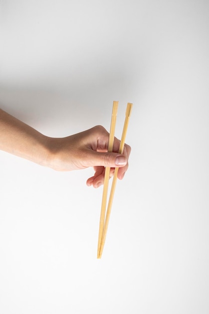 Mano della donna che tiene due bacchette cinesi su sfondo bianco