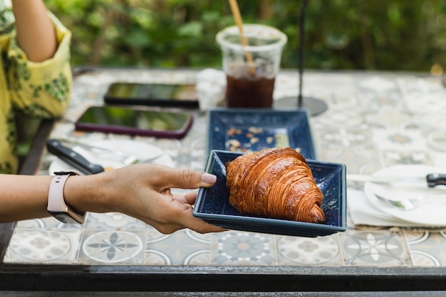 Mano della donna che tiene i croissant sulla tavola in caffè all'aperto