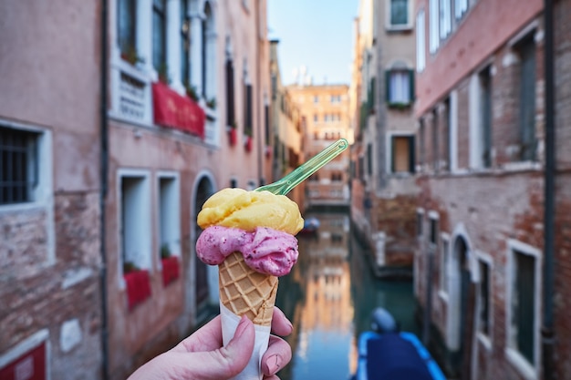 Mano della donna che tiene il cono gelato gelato italiano sul ponte a Venezia, Italia.