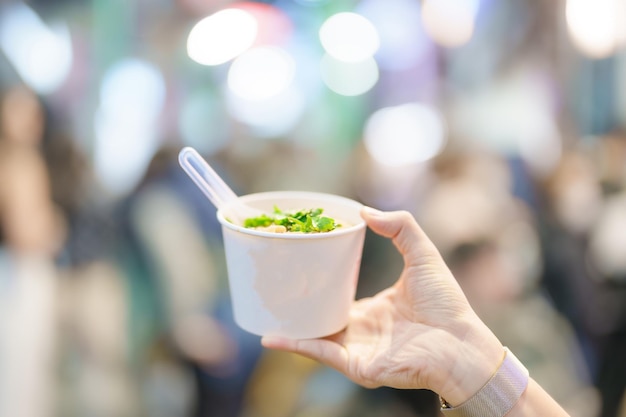 Mano della donna che tiene la tagliatella di riso in ciotola di carta al mercato notturno di Ximending famoso cibo di strada taiwanese di cibo esotico di Taiwan nel mercato locale