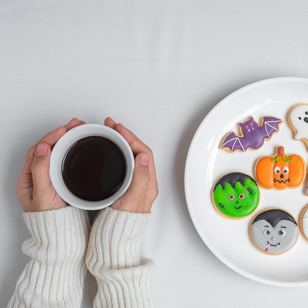 Mano della donna che tiene la tazza di caffè durante il consumo di divertenti biscotti di Halloween Felice giorno di Halloween Dolcetto o minaccia Ciao ottobre autunno autunno festa tradizionale e concetto di vacanza