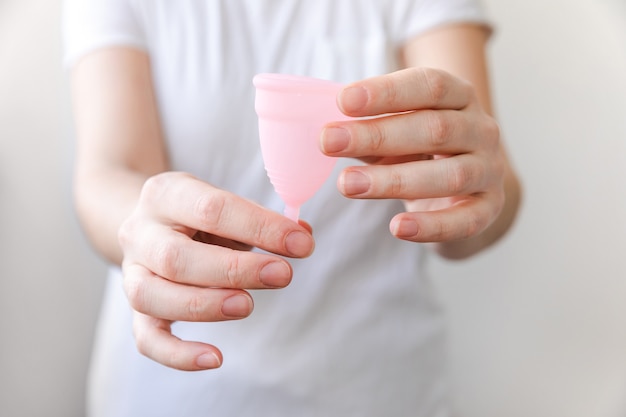 Mano della donna che tiene la tazza mestruale rosa isolata su fondo bianco. Donna moderna alternativa eco igiene ginecologica nel periodo mestruale. Contenitore per sangue in mano della ragazza.