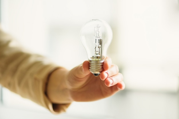 Mano della donna che tiene lampadina su priorità bassa crema con lo spazio della copia. Idea creativa, nuovo piano aziendale, motivazione, innovazione, concetto di ispirazione.