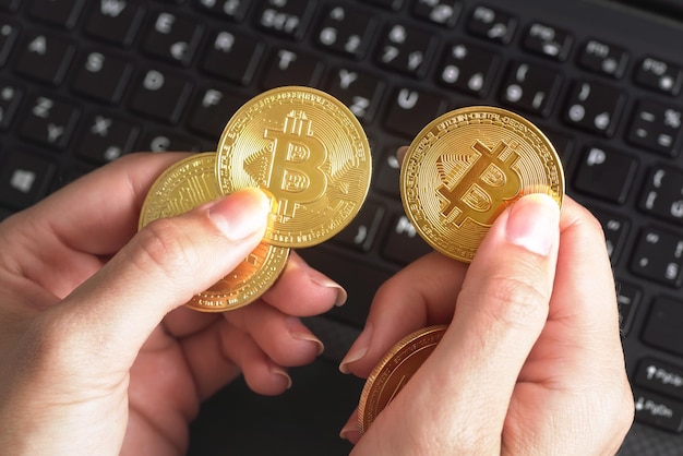 Mano della donna che tiene monete bitcoin di colore dorato sopra la tastiera nera del computer portatile