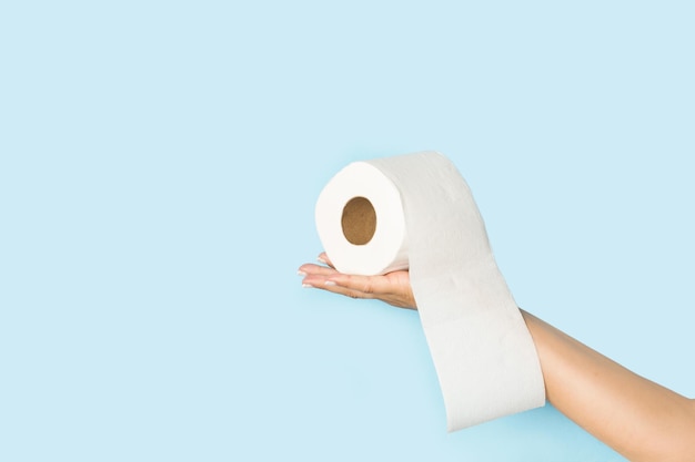 Mano della donna che tiene un rotolo di carta igienica su uno sfondo azzurro con spazio per la copia