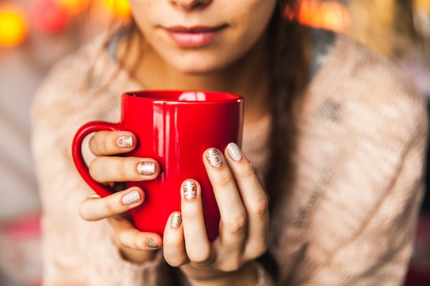 Mano della donna che tiene una tazza di caffè rossa. Con una bella manicure invernale. Bere, moda, mattina