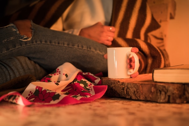 Mano della donna che tiene una tazza su un ceppo di legno in una fredda notte d'inverno