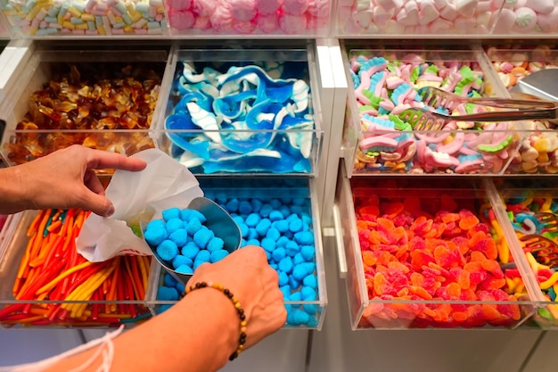 Mano della donna con la paletta che prende le caramelle deliziose colorate sul bancone del caffè del mercato della drogheria del negozio