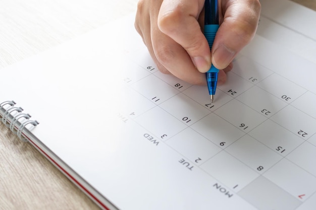 Mano della donna con la scrittura della penna sul concetto di riunione dell'appuntamento di pianificazione aziendale della data del calendario