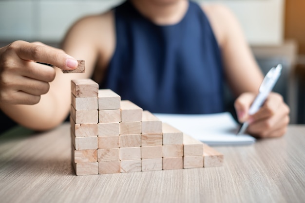 Mano della donna di affari che dispone o che tira blocco di legno sull&#39;edificio.