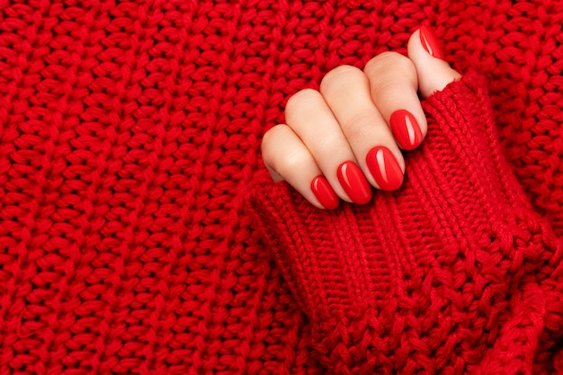 Mano della donna in maglione con manicure rosso su grigio