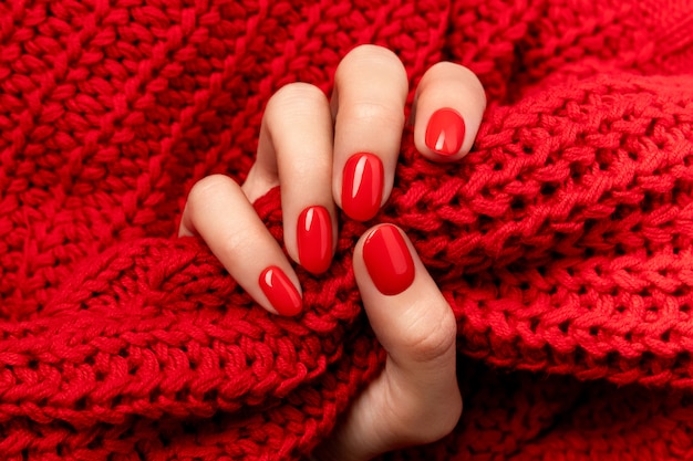 Mano della donna in maglione con manicure rosso su grigio