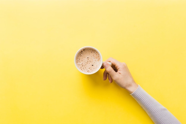 Mano della donna in stile minimalista che tiene una tazza di caffè su sfondo colorato Vista dall'alto vista dall'alto della tazza da cappuccino Posto vuoto per lo spazio della copia del testo Dipendenza dal caffè Vista dall'alto disposizione piatta