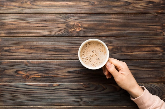 Mano della donna in stile minimalista che tiene una tazza di caffè su sfondo colorato Vista dall'alto vista dall'alto della tazza da cappuccino Posto vuoto per lo spazio della copia del testo Dipendenza dal caffè Vista dall'alto disposizione piatta