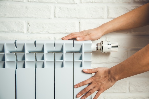 Mano della donna nel radiatore caldo sul fondo del muro di mattoni