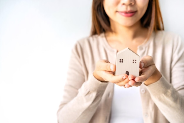 Mano della giovane donna che tiene il modello di casa in legno Concetto di bene immobile