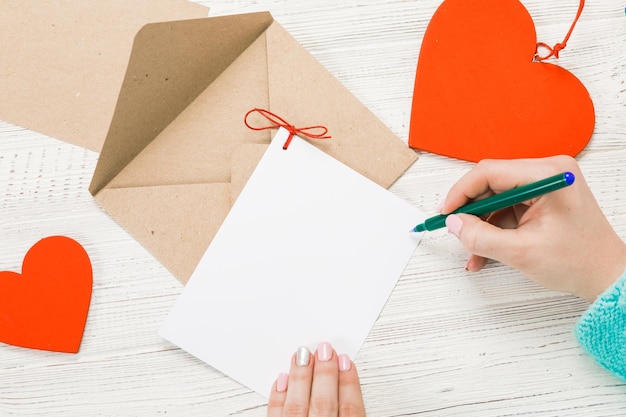 Mano della ragazza che scrive lettera d'amore il giorno di San Valentino Cartolina fatta a mano con figura a forma di cuore rosso 14 febbraio festa di San Valentino concetto con spazio di copia