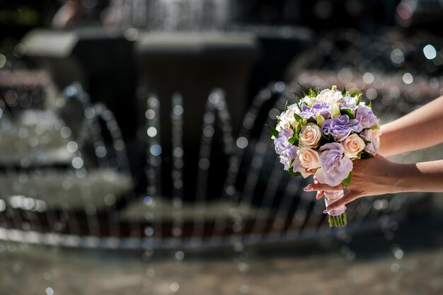 Mano della sposa che tiene il bouquet da sposa su una fontana