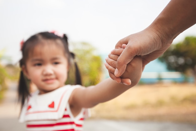 Mano della tenuta della ragazza del bambino asiatico e del genitore insieme con amore e cura