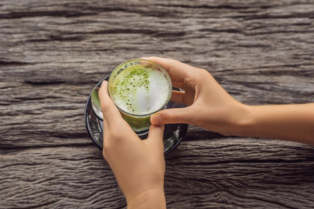 Mano delle donne che tiene una tazza di matcha Latte, tè verde, sul vecchio tavolo di fondo in legno.