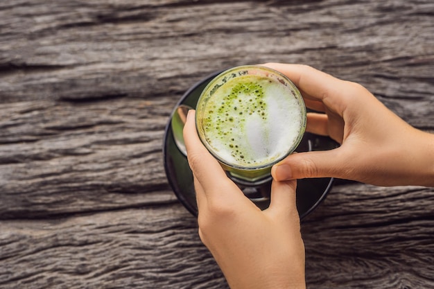 Mano delle donne che tiene una tazza di matcha Latte, tè verde, sul vecchio tavolo di fondo in legno.