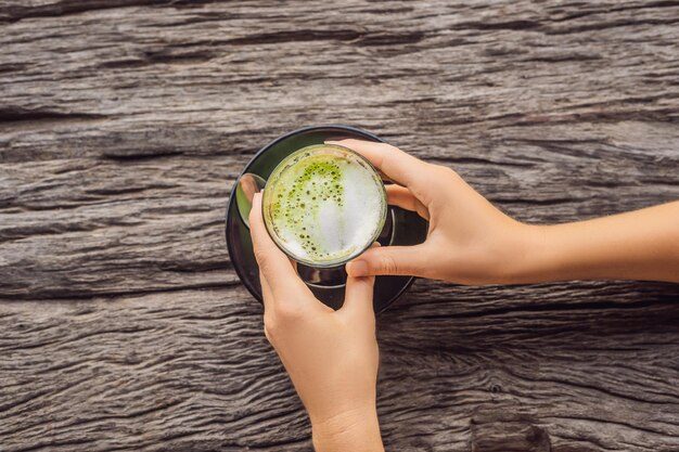 Mano delle donne che tiene una tazza di matcha Latte, tè verde, sul vecchio tavolo di fondo in legno.