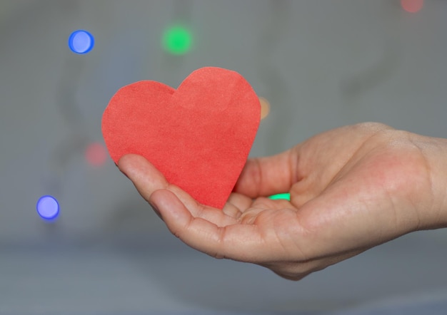 mano delle ragazze che tiene le luci di Natale del cuore di carta rossa sullo sfondo