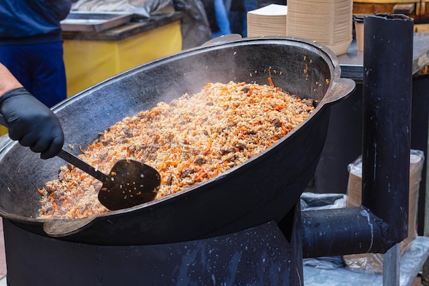 Mano dello chef in guanto nero che cucina piatto di carne palov sul forno all'aperto in strada Cibo per senzatetto