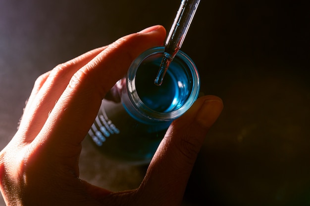 Mano dello scienziato che tiene il pallone con vetreria da laboratorio e provette in background di laboratorio chimico