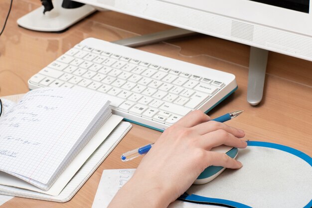 Mano dello studente con un mouse e una tastiera di computer con un taccuino e una penna.