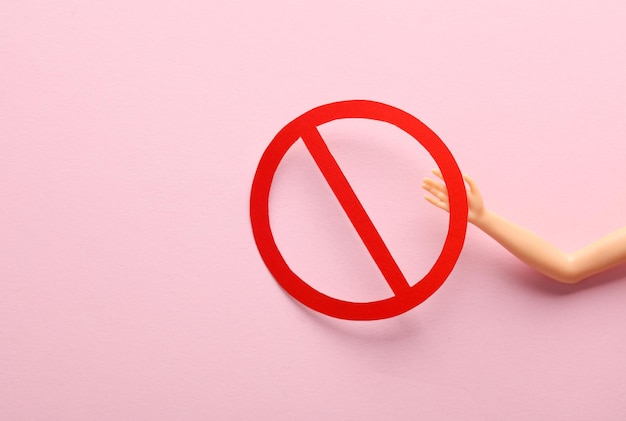 Mano di bambola con segno di proibizione su sfondo rosa